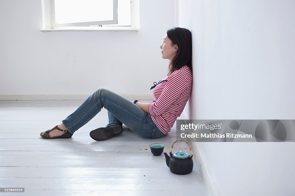 Young woman sitting on floor with kettle and tea cup beside her