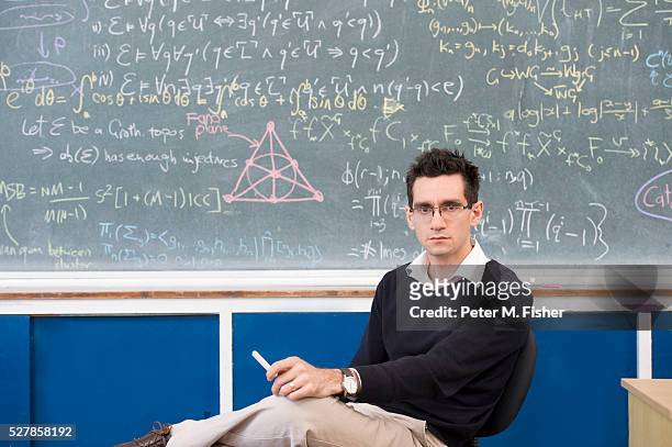 portrait of young man sitting by blackboard - professor stock-fotos und bilder