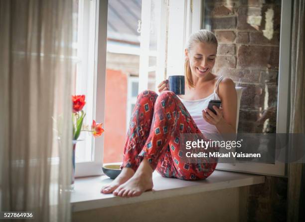 young woman sitting in pyjamas on windowsill - pajamas stock pictures, royalty-free photos & images