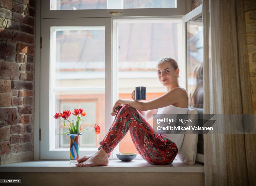 Young woman sitting in pyjamas on windowsill