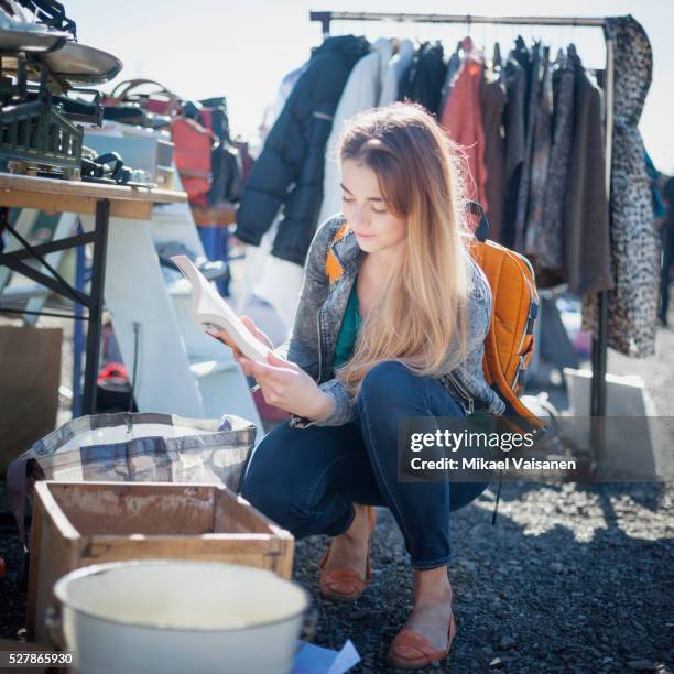 young woman on flea market looking through displayed products - flea market stockfoto's en -beelden