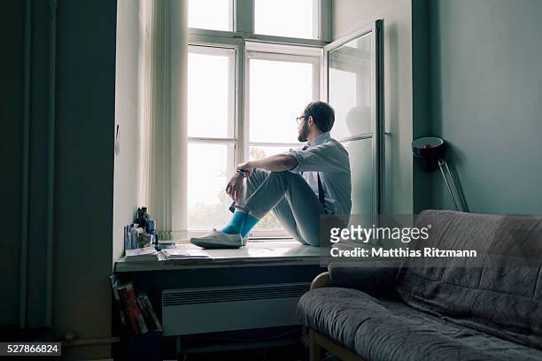 man sitting on window sill - aspettare foto e immagini stock