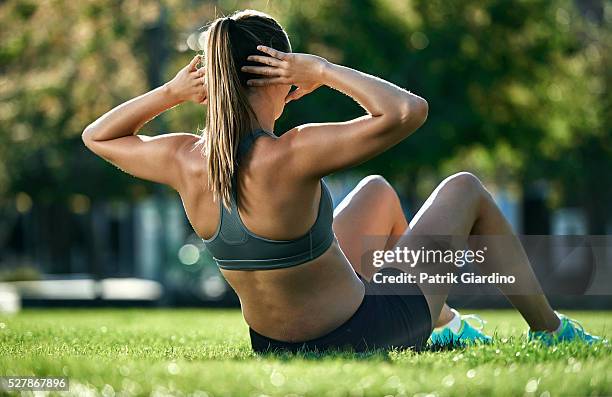 young woman doing sit-ups in park - sit up foto e immagini stock