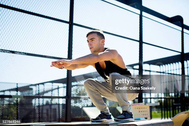 young man squatting outdoors - hockend stock-fotos und bilder