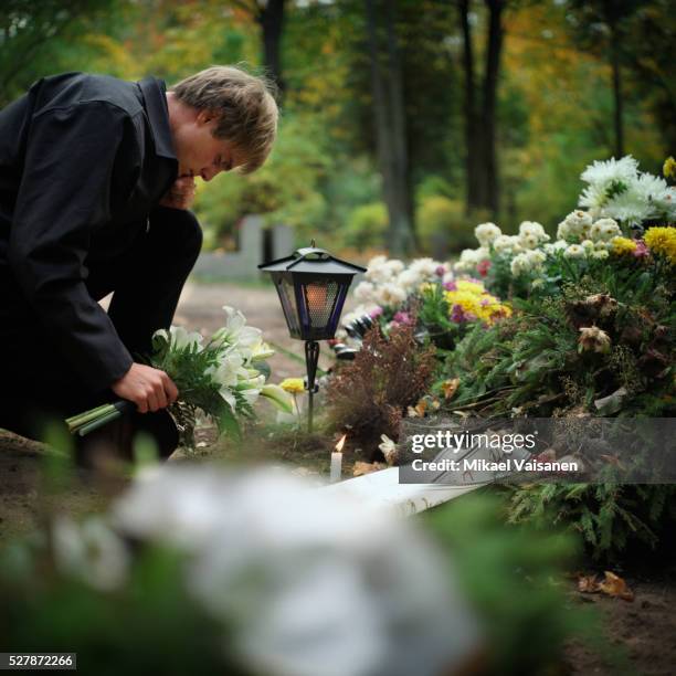 young man putting flowers on grave - mourning flowers stock pictures, royalty-free photos & images