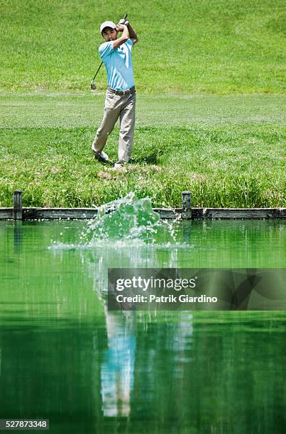 young man plying golf with ball falling in pond - golf ball in air stock pictures, royalty-free photos & images