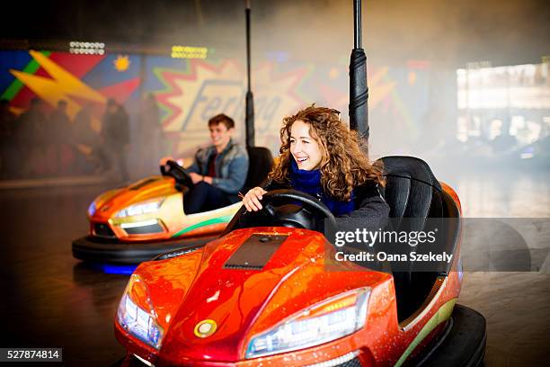 young couple driving bumper cars in amusement park - amusement park ride stock pictures, royalty-free photos & images