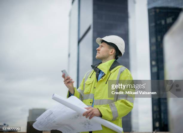 architect on high rise construction site with blueprints - plan architecte photos et images de collection