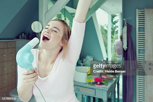 young woman in bathroom singing into hairdryer - singing fotografías e imágenes de stock