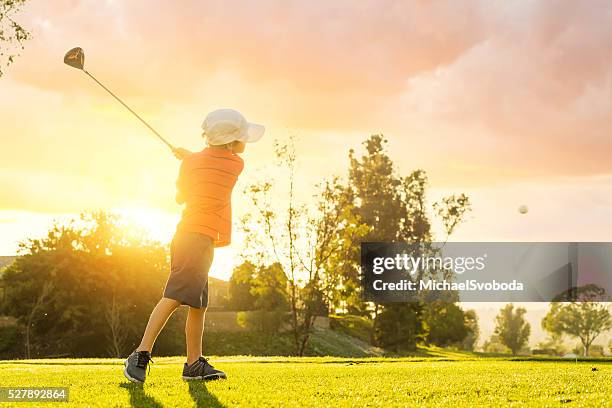 young boy golfer teeing off during sunset - junior stock pictures, royalty-free photos & images