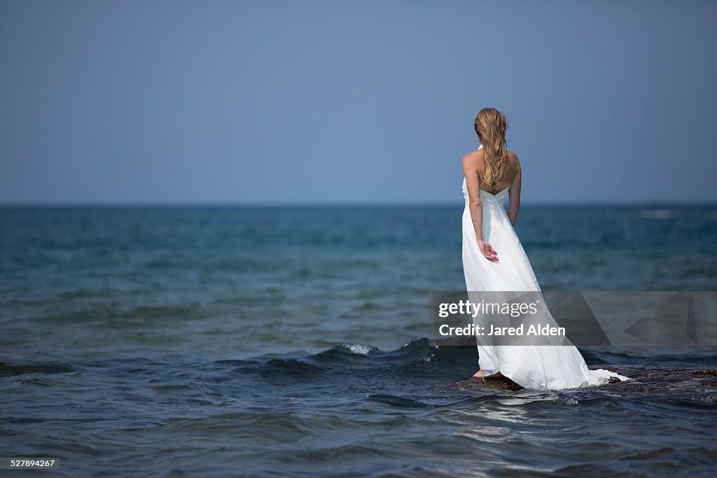 Woman in White Dress on Rock admits Blue Water