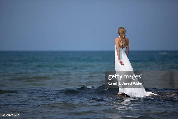 woman in white dress on rock admits blue water - white dress stock pictures, royalty-free photos & images