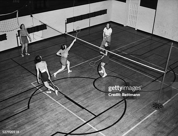 Overhead view of an indoor badminton game. Four women are playing, one observes. Undated photograph, circa 1950's.
