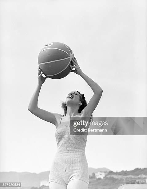 Woman stands in a bathing suit holding a beach ball above her head. Undated photograph, circa 1950's.