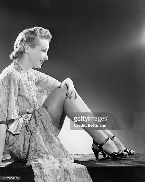 Hilarry Brooks sits on the floor with her legs tucked. She wears a silk robe and high heels. The robe is open to reveal the top of her thigh-high...
