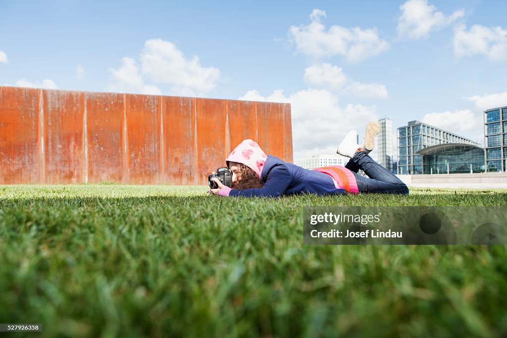 Young creative person laying on gras and taking picture with camera