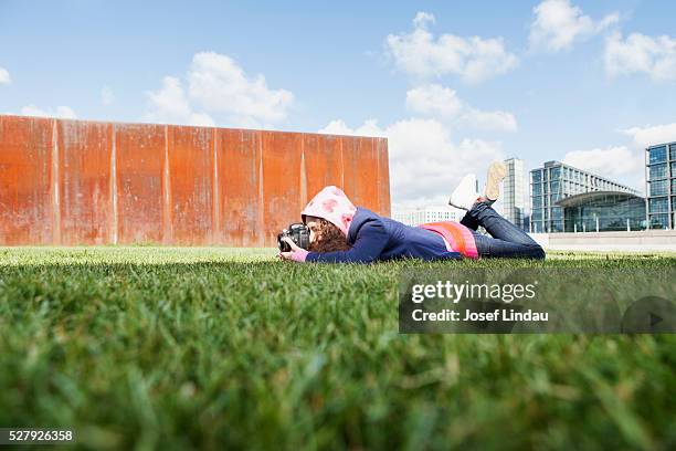 young creative person laying on gras and taking picture with camera - josef lindau stock-fotos und bilder