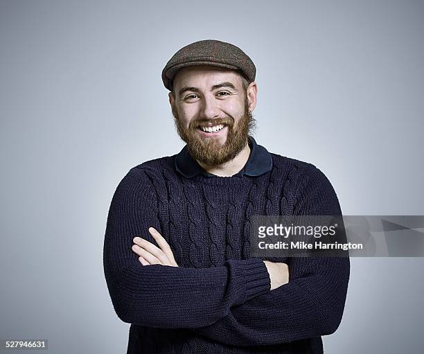 bearded man wearing jumper and flat cap smiling - flat cap stock pictures, royalty-free photos & images