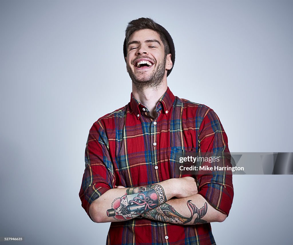 Tattooed young male in check shirt laughing.