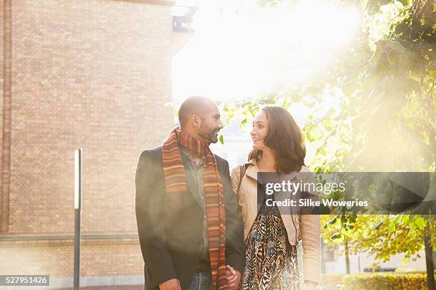 portrait of a couple walking along a path and chatting with the flares of sunshine surrounds them - man and woman holding hands profile stockfoto's en -beelden