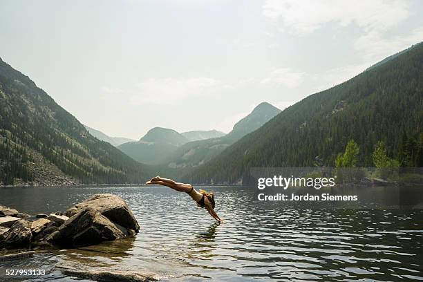 a woman diving off a rock. - mountain side stock pictures, royalty-free photos & images