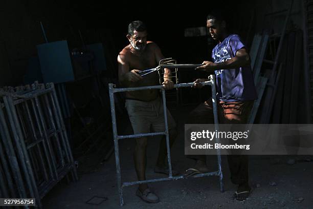 Two men fix a piece of scaffolding at an equipment rental shop in Itaborai, Brazil, on Tuesday, April 12, 2016. Just 30 miles east of the bustling...