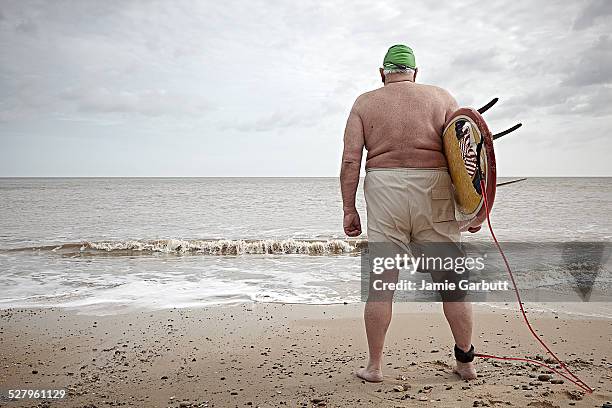 elderly overweight surfer with back to camera - fat guy on beach fotografías e imágenes de stock