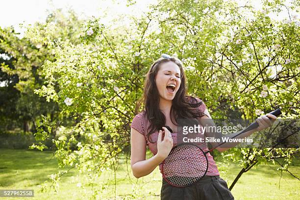 young adult woman playing air guitar with a badminton racket - summer sounds stock-fotos und bilder