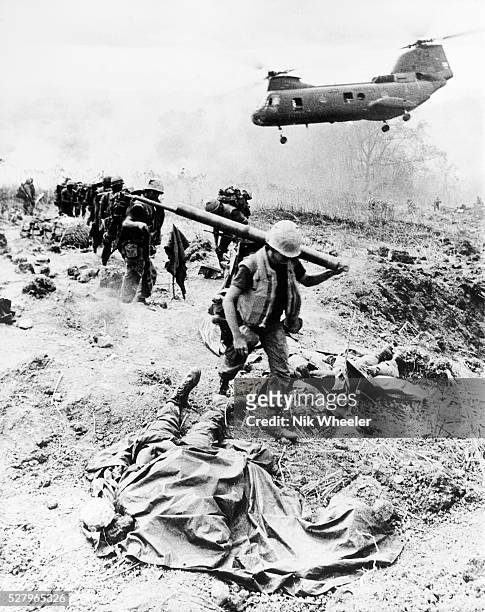 United States Marine troops on operation near the Demilitarized Zone in I Corps near the border with North Vietnam walk past covered body of dead...