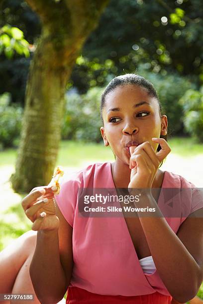 portrait of a young african woman sitting under a tree eating a sandwich - paradise jam stock pictures, royalty-free photos & images