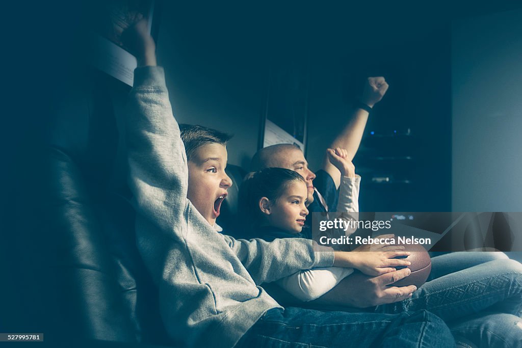 Father, son and daughter watching football game