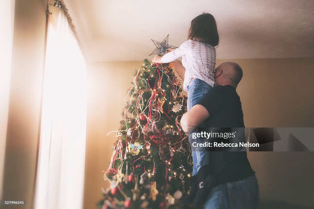 Father helping daughter put star on Christmas tree