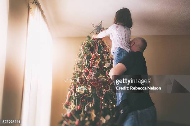 father helping daughter put star on christmas tree - decorare l'albero di natale foto e immagini stock