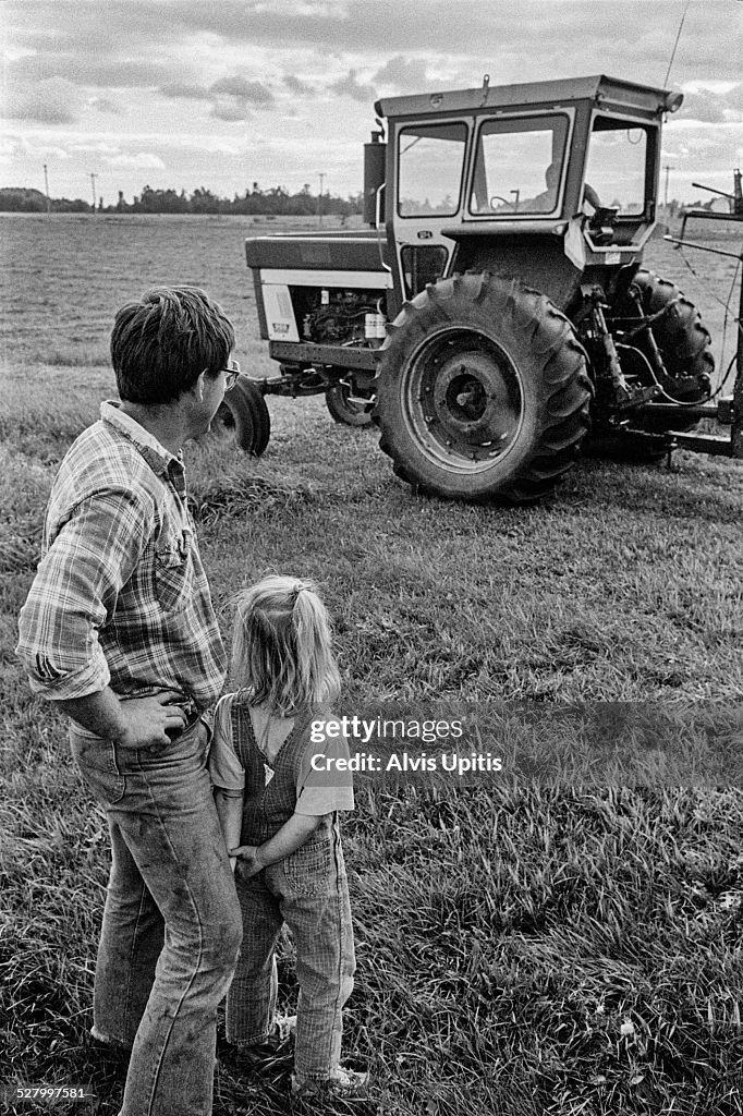 Father and daughter watch son work tractor