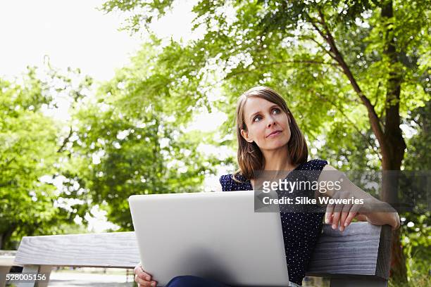 portrait of content middle-aged woman working on laptop in park - bench park stock-fotos und bilder