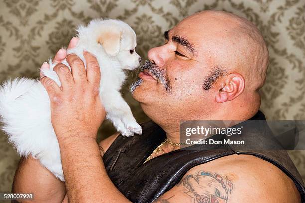 tattooed man cuddling with a puppy - juxtaposition stock-fotos und bilder