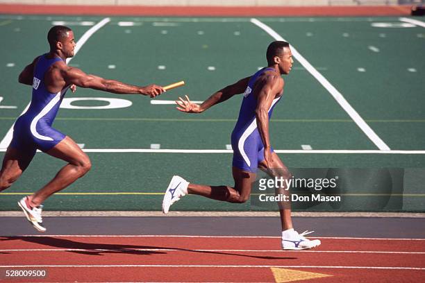 relay racers handing-off baton - relay race stock pictures, royalty-free photos & images