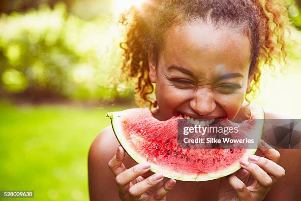 portrait of a young woman eating watermelon on a sunny day, backlit - woman eating fruit stock-fotos und bilder
