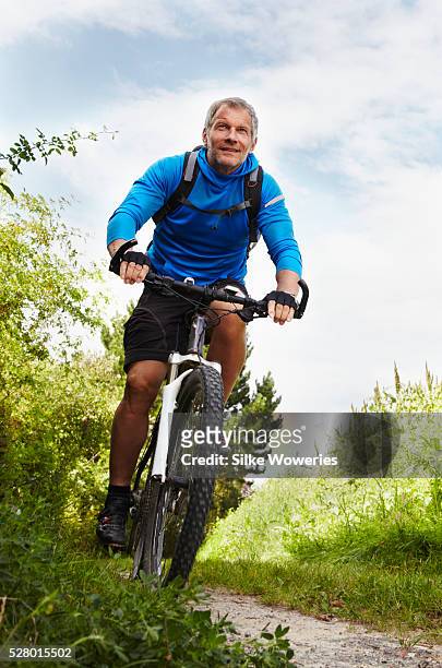 active middle-aged man cycling outdoors on a mountain bike - 50 59 years stock pictures, royalty-free photos & images