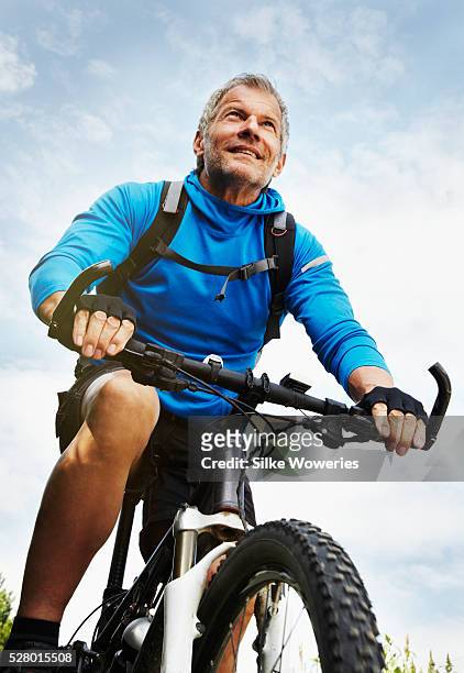 active middle-aged man cycling outdoors on a mountain bike - age 55 health stock pictures, royalty-free photos & images