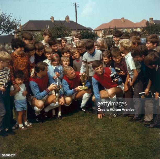 Crowd gathered around the three West Ham footballers, left to right, Geoff Hurst, Bobby Moore and Martin Peters, who are each holding a trophy, 16th...
