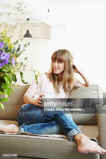 content mid-adult woman sitting at home on the sofa drinking tea - 30 39 years stock pictures, royalty-free photos & images