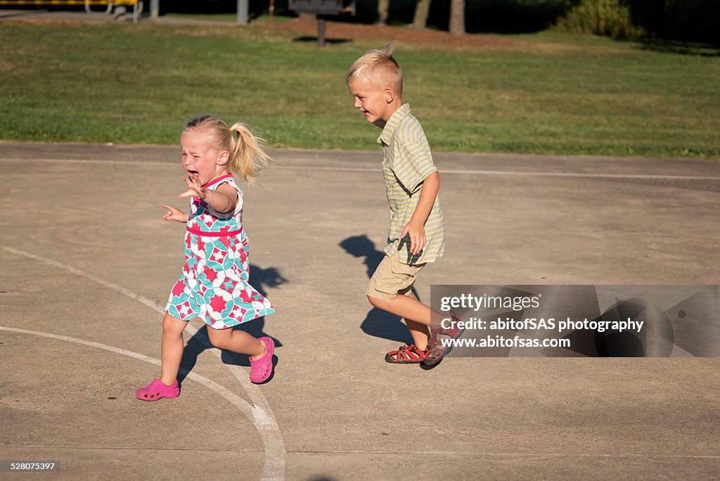 Young boy chases his crying toddler sister