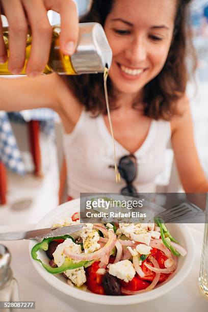 happy woman pouring oil into salad - feta stock-fotos und bilder