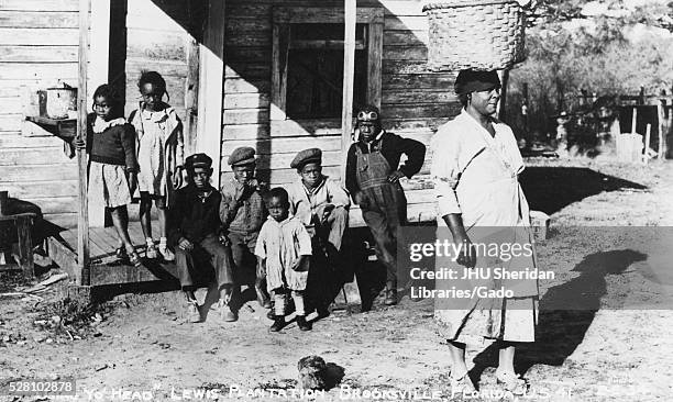 Group of seven young African American children with serious expressions are gathered on the porch of a shanty on the Lewis Plantation in Brooksville,...