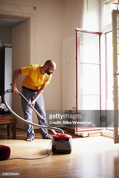 young adult man cleaning his flat with a vacuum cleaner. - house husband stock pictures, royalty-free photos & images