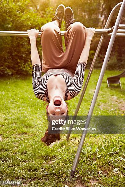 portrait of young adult woman hanging upside down on jungle gym - girl upside down stock pictures, royalty-free photos & images