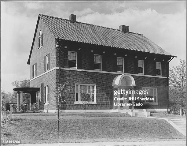 Photograph of the exterior of a brick home in Baltimore, Maryland featuring windows with and without shutters, chimneys, and two small sets of stairs...