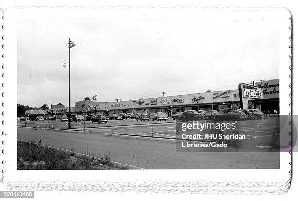 Photograph of the parking lot for the Northwood Shopping Center in Baltimore, Maryland, showing cars and commercial buildings such as Singer, S S...