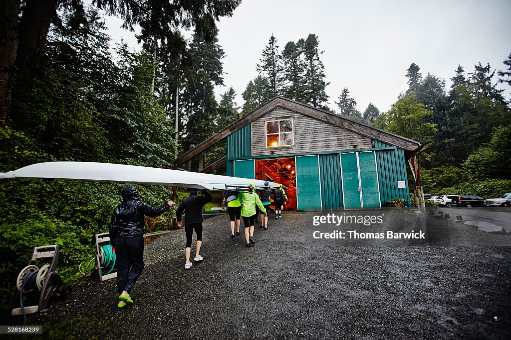 Female rowers carrying rowing shell into boathouse